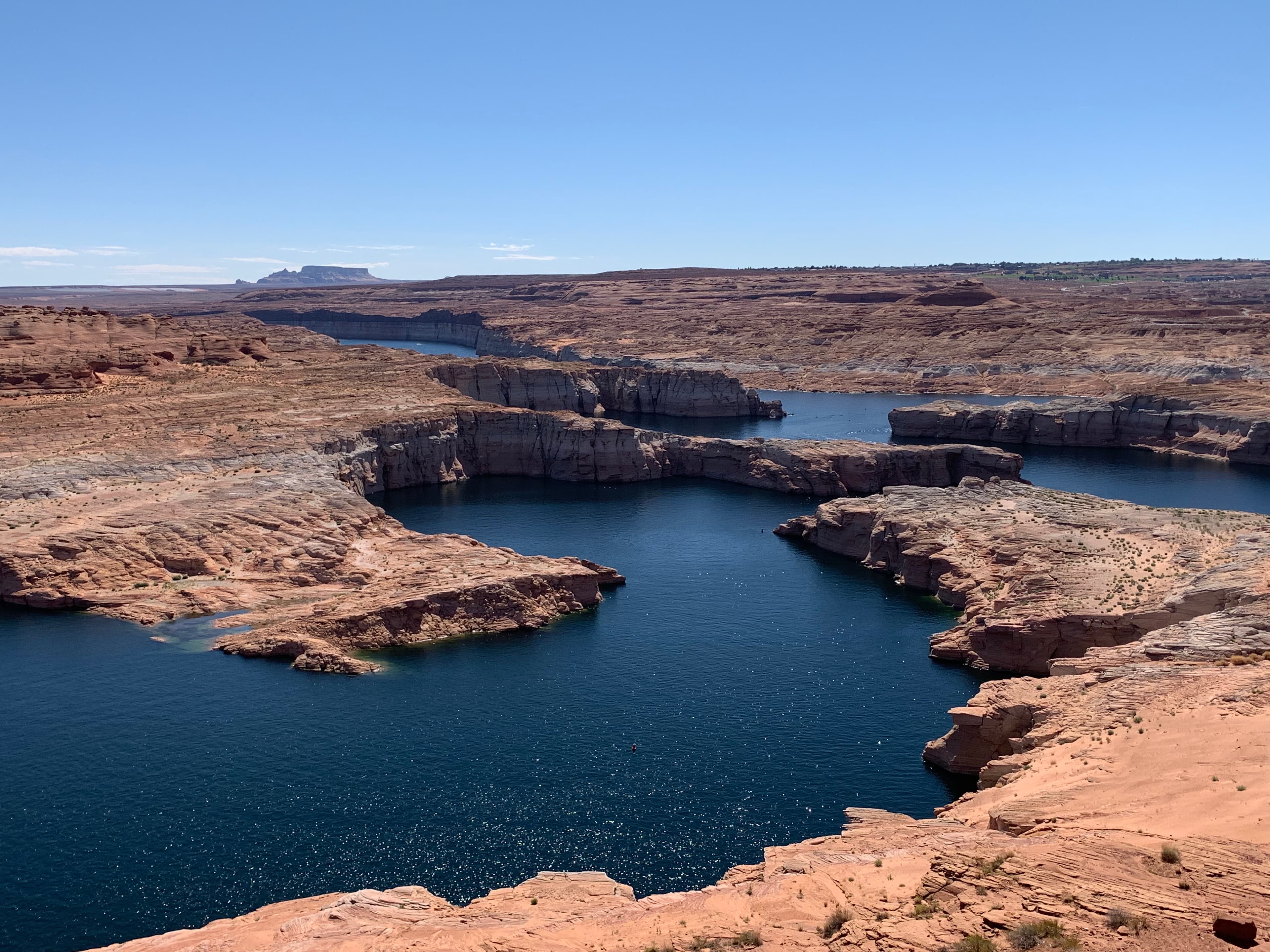 Lake Powell viewed from an elevated red-rock overlook, with the main channel winding between sandstone terraces toward Tower Butte in the distance