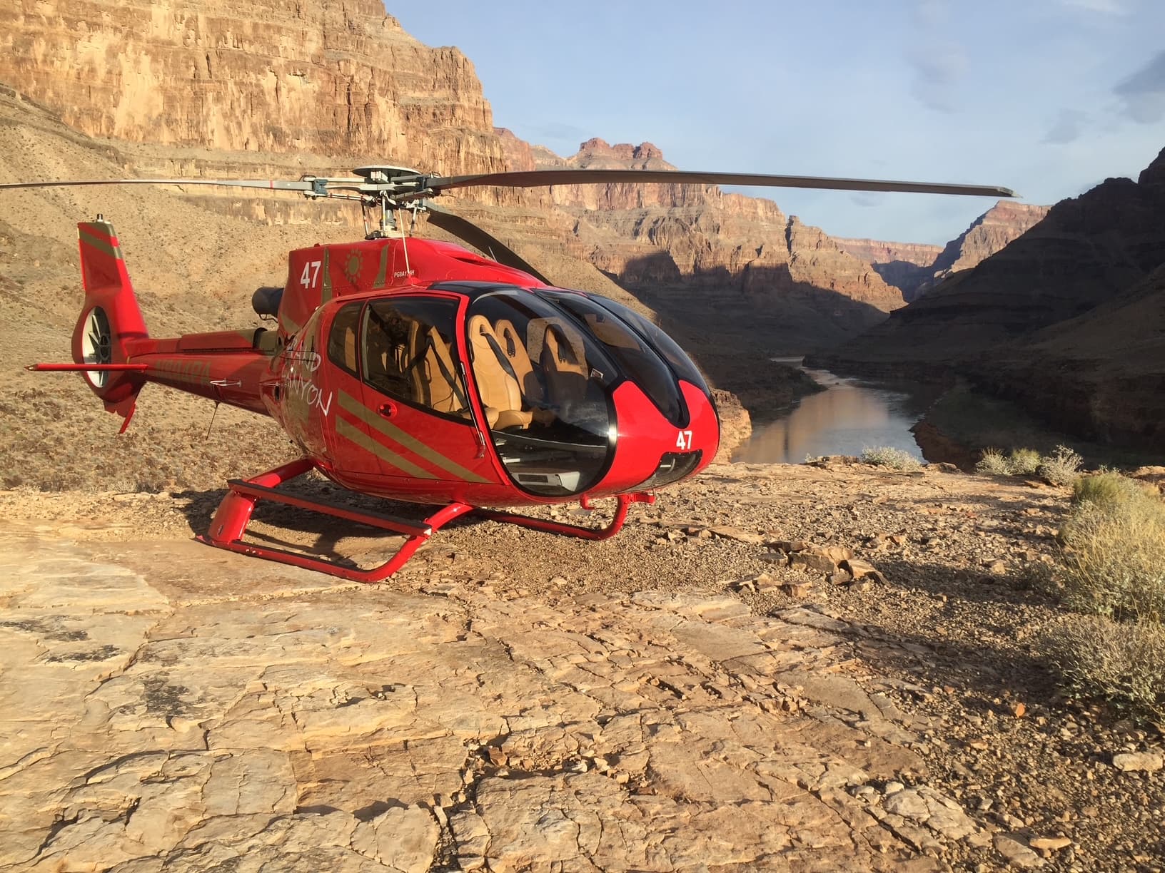 Papillon EC130 helicopter parked on the rocky canyon floor at the Grand Canyon West Rim landing zone, Colorado River visible in the background